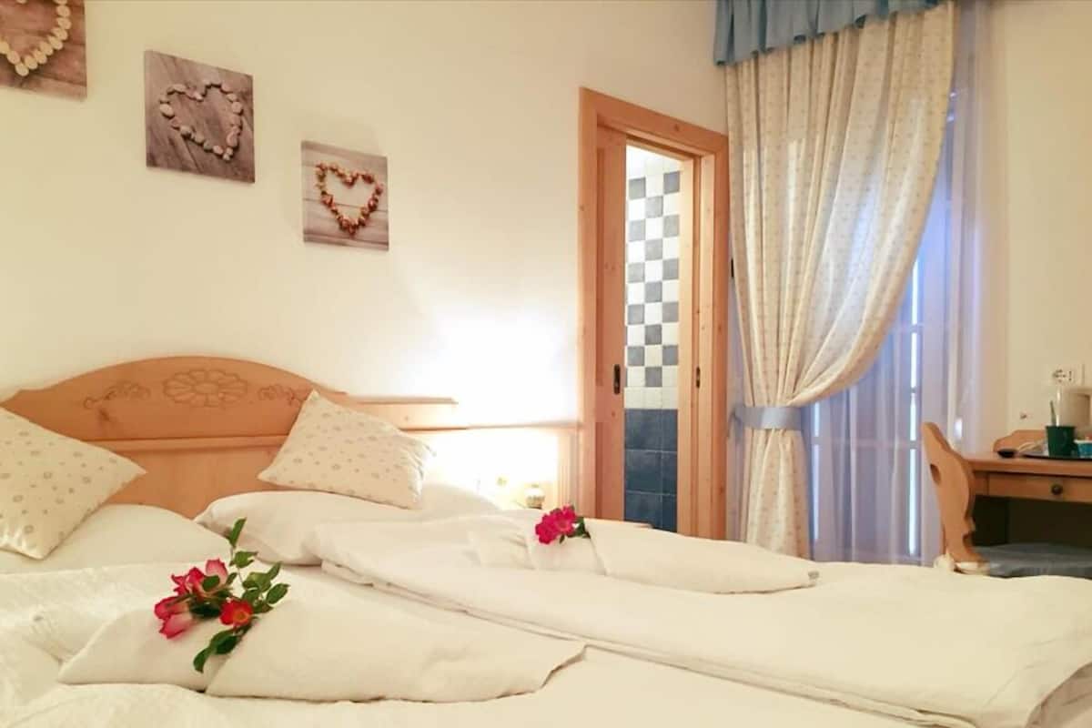 Ein ordentlich bezogenes Bett mit weißen Leinen und einer einzelnen roten Rose, ein hölzernes Kopfende und ein kariertes Muster an der Wand.