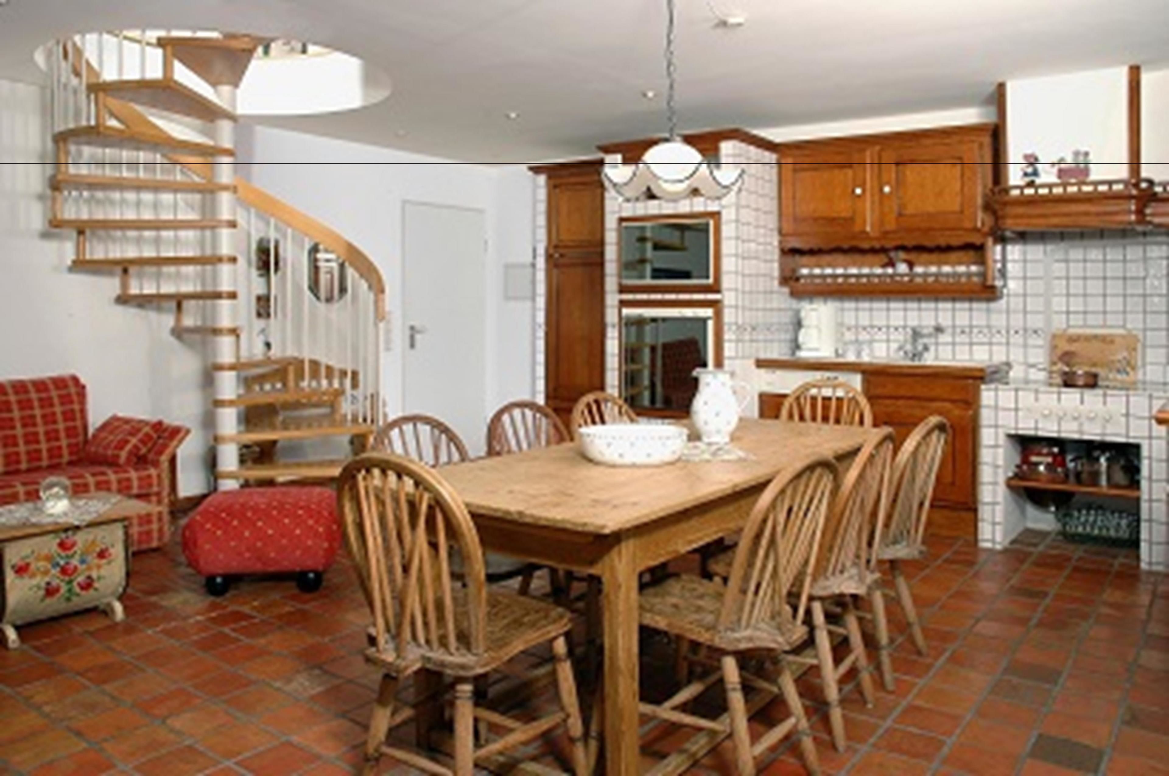 A dining area with a wooden table and chairs, a kitchen with wooden cabinets, and a spiral staircase.