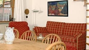 A living room with a red plaid sofa, wooden chairs, a table with a pitcher, and a painting on the wall. - Ferienwohnungen Schencking (Reit im Winkl)