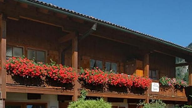 A wooden building with multiple balconies, each adorned with red flowers. - Ferienwohnungen Schencking (Reit im Winkl)