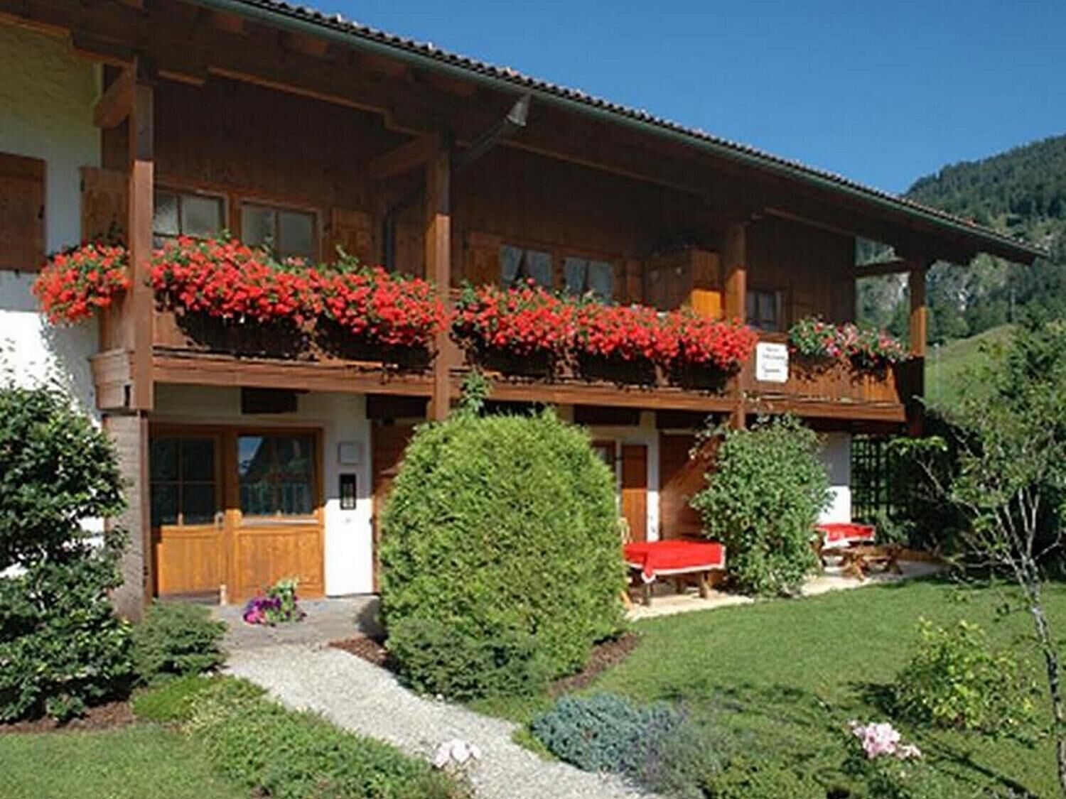 Een houten chalet met balkons versierd met rode bloemen, een houten deur en een verzorgde tuin.