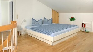 A bedroom with a bed, wooden flooring, a crib, a nightstand, and a small plant. - Ferienwohnungen Schencking (Reit im Winkl)