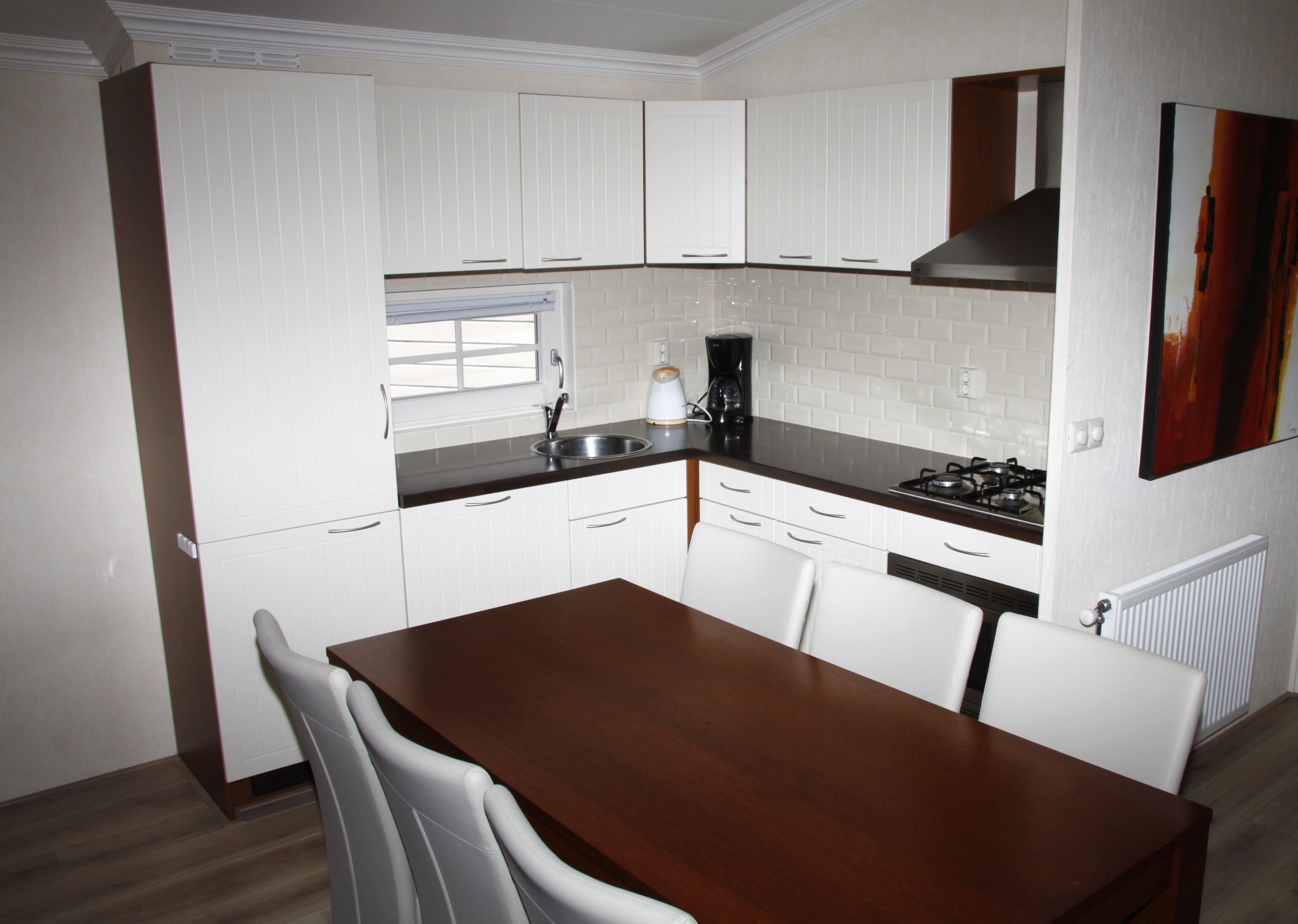 A kitchen with white cabinets, a dark countertop, a gas stove, and a window with blinds.