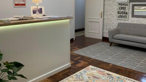 Un'area reception di un hotel con una scrivania, una lampada, un orologio, una targa incorniciata, un divano e un tappeto a motivi.