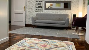 Un soggiorno moderno con un divano grigio, un tappeto decorato e una parete con specchi ornamentali e una insegna.