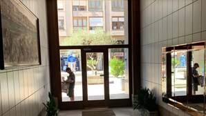 Un'accogliente hall moderna, con pavimento piastrellato, un'ampia opera d'arte incorniciata a sinistra e una porta in vetro che dà sull'esterno.