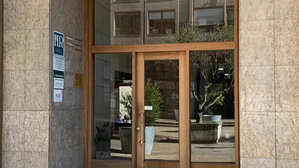 Ingresso di un edificio con una porta in legno, una vetrina e un cartello che vieta i giochi con la palla.
