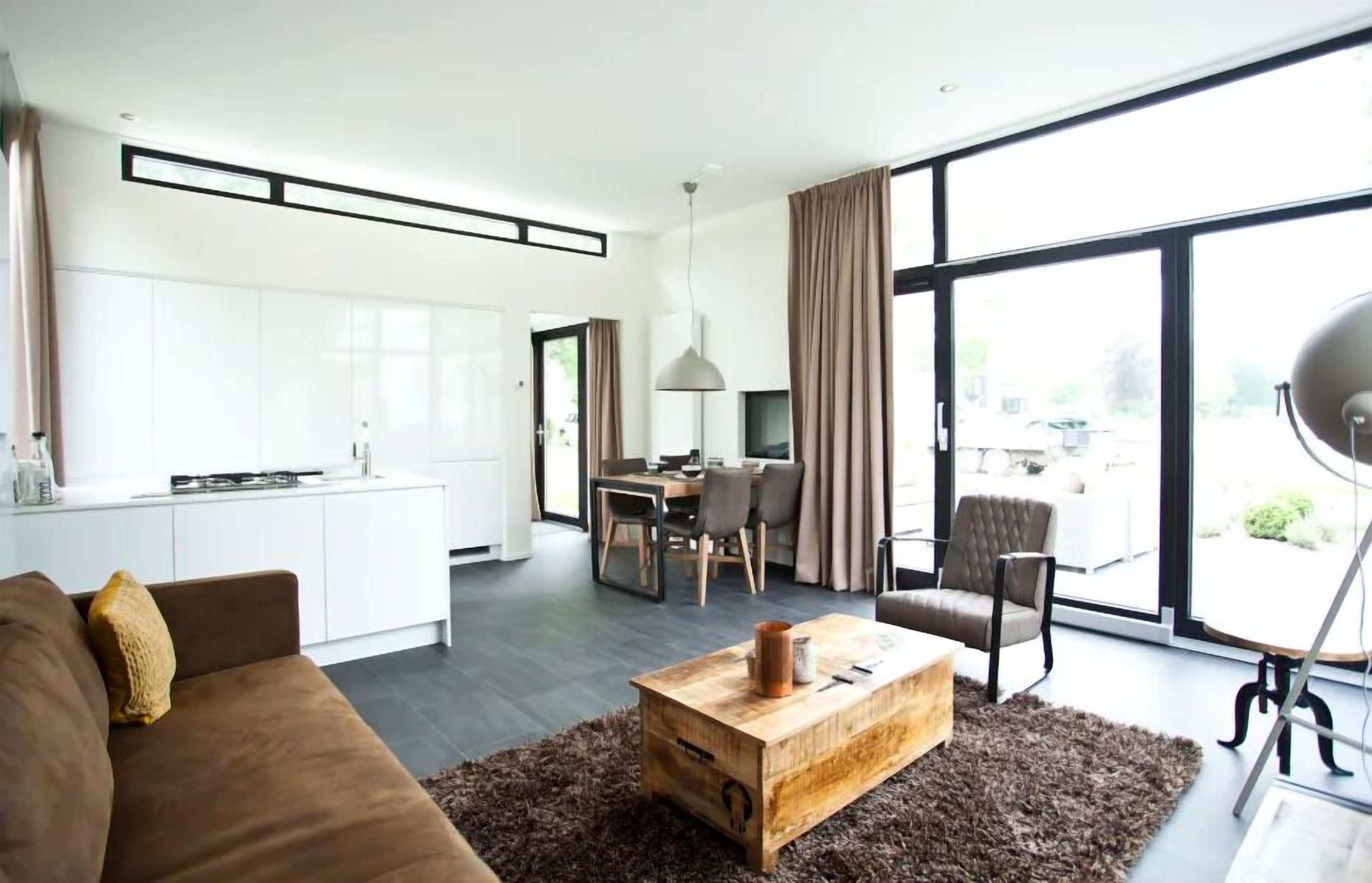 Uma sala de estar moderna com um sofá marrom, uma mesa de centro de madeira e uma área de jantar com mesa e cadeiras.