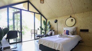 A modern bedroom with a large bed, a desk, and a chair. There is a large window providing natural light and a view of greenery outside. - EuroParc De Zanding (Otterlo)