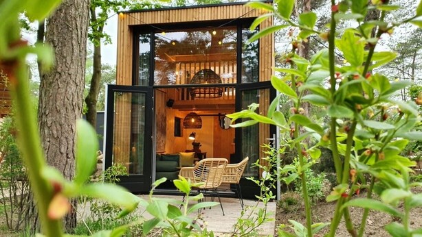 A modern, glass-walled cabin with a cozy interior, surrounded by lush greenery. - EuroParc De Zanding (Otterlo)