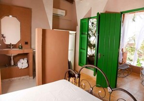 Une chambre avec un lit, une salle de bain avec un lavabo et une porte verte donnant sur un espace extérieur aménagé avec des chaises.
