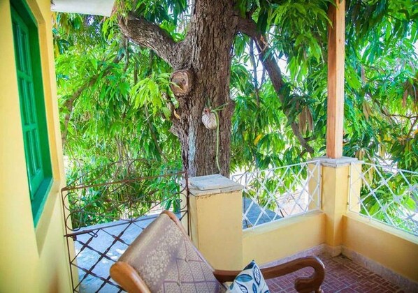 A balcony with a chair, a tree, and a view of lush greenery. - Casa Gardenia's (Trinidad)