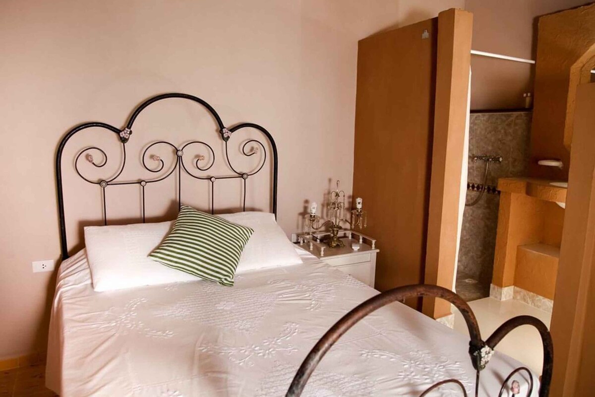 Un lit bien fait, avec une tête de lit en métal, une table de chevet avec une lampe et une armoire en bois.