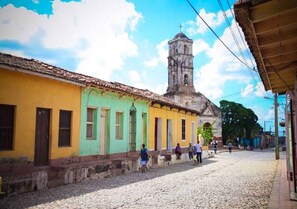 A cobblestone street with colorful buildings and a church tower in the background. - Casa Gardenia's (Trinidad)