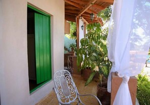 A covered patio with a green door, potted plants, and a metal chair. - Casa Gardenia's (Trinidad)