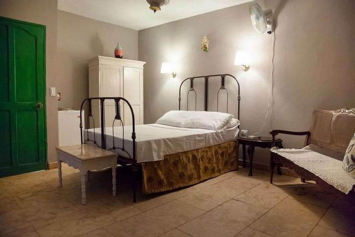 Une chambre à coucher avec un lit, une table de chevet, une chaise, une armoire et une porte verte.