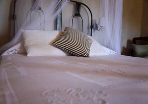 A neatly made bed with a white bedspread and a striped pillow, a metal headboard, and a white curtain. - Casa Gardenia's (Trinidad)