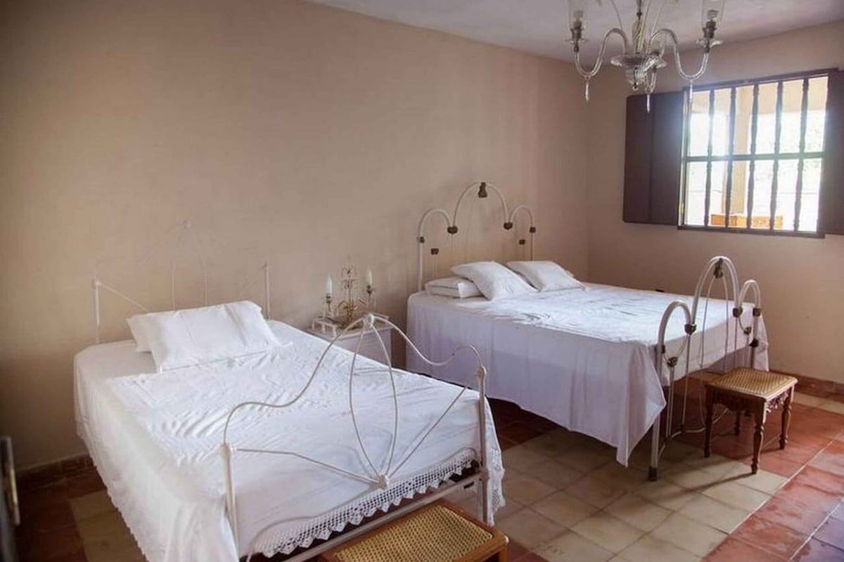 Une chambre avec deux lits, un lustre, une fenêtre et une petite table.