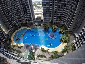 A high-rise building with a large swimming pool featuring dolphin designs, surrounded by palm trees and lounge areas. - Line Friends Homestay Atlantis Melaka (Malacca City)