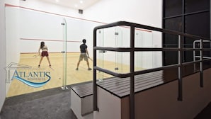 Uma quadra de squash com paredes de vidro, piso de madeira e guarda-corpo de metal.