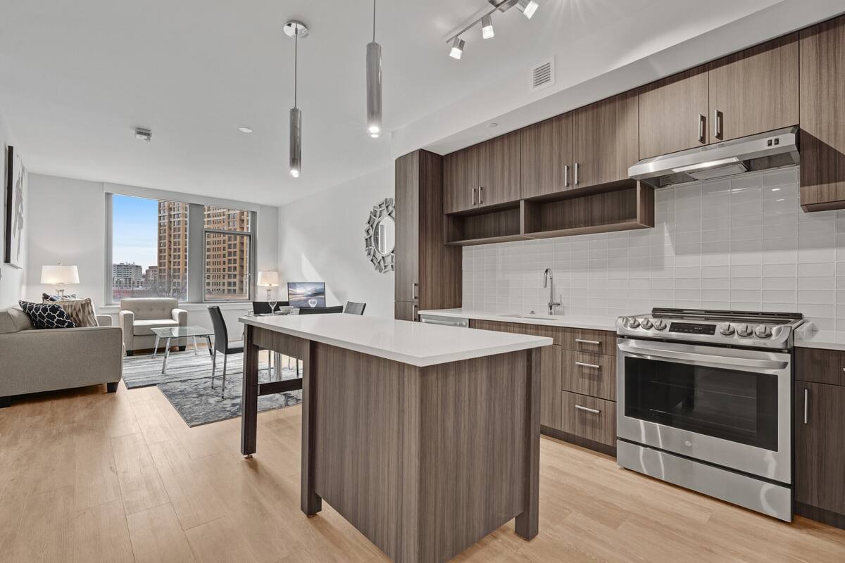 A modern kitchen with a central island, stainless steel appliances, and a view of the city through large windows.