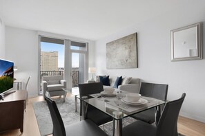 Un salon moderne avec une table à manger en verre, des sièges confortables, une grande fenêtre et une vue sur la ville.
