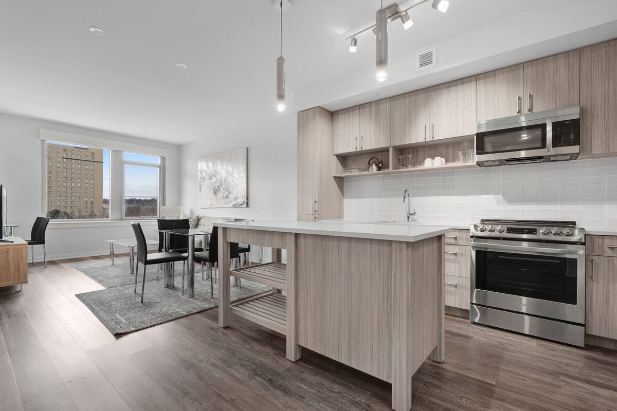 A modern kitchen with a central island, stainless steel appliances, and light wood cabinetry.