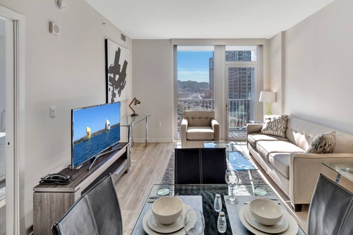 A modern living room with a television, a dining table set with plates and glasses, a sofa, and a chair.