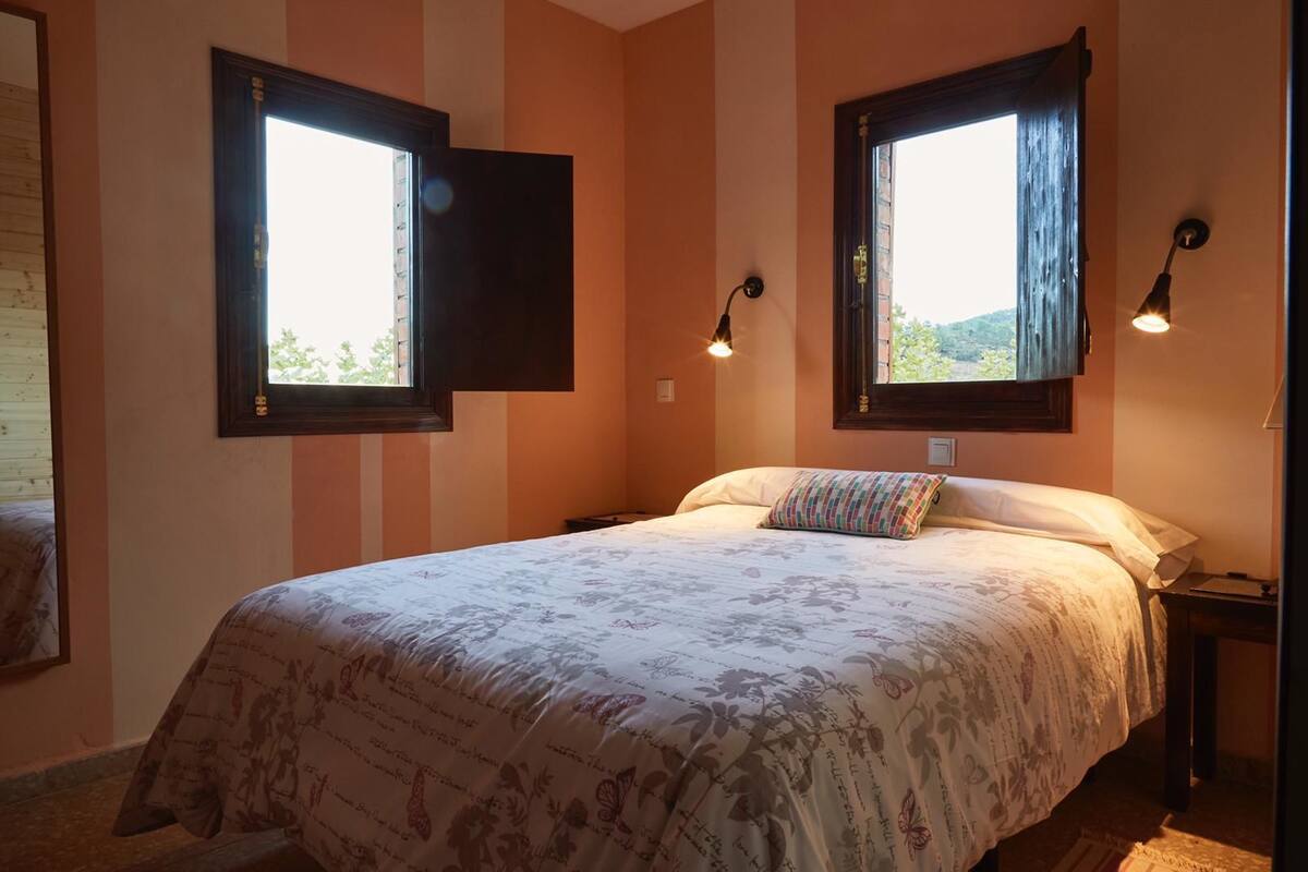A bedroom with a bed, two windows, and two wall-mounted lamps.