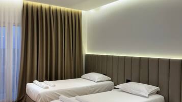 Hotellihuone, jossa on kaksi sänkyä, suuri ikkuna läpikuultavilla verhoilla ja moderni kattorakenne.