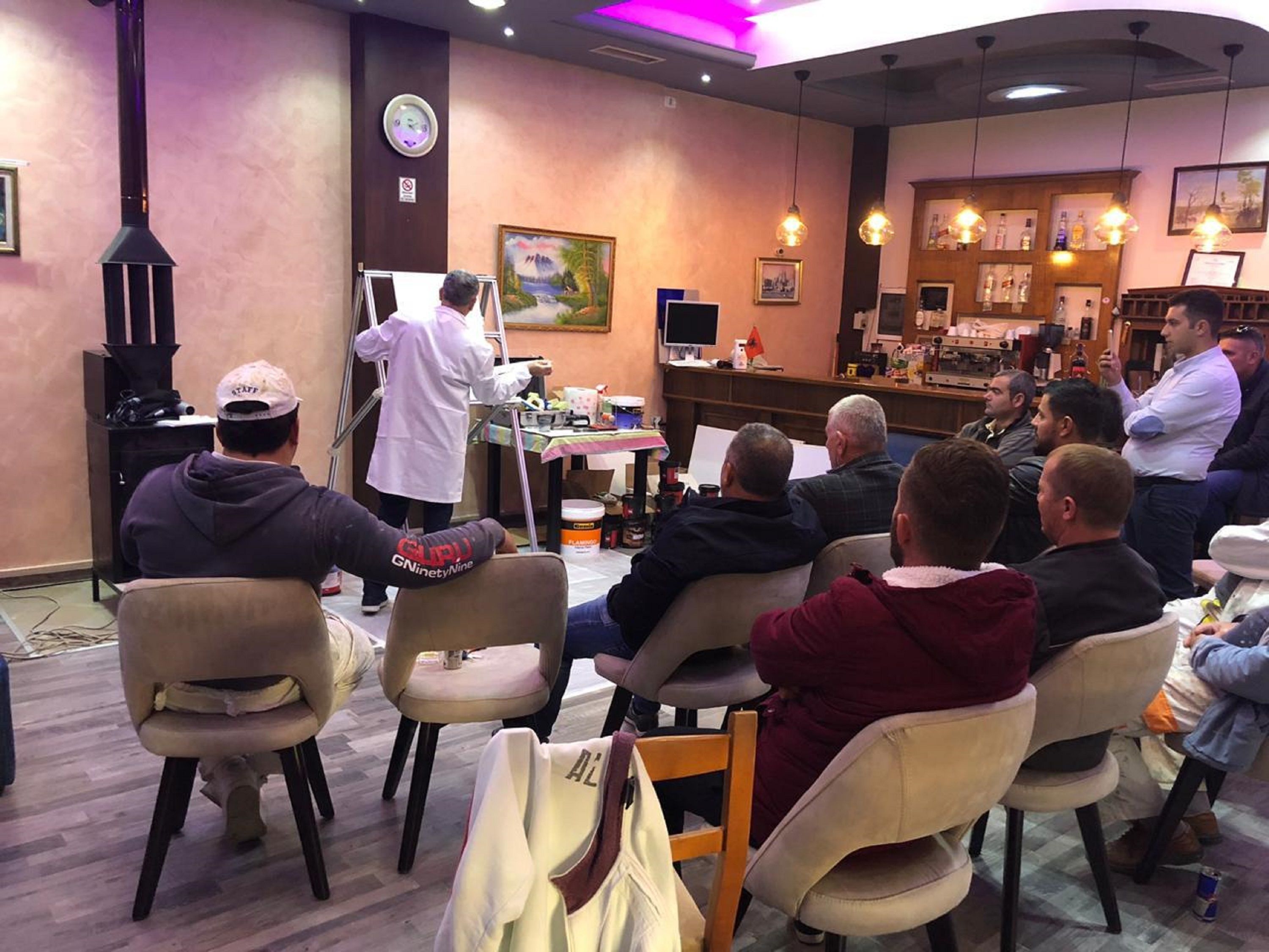 Een groep mensen zit in een kamer, met een bar op de achtergrond.