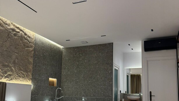 A modern bedroom with a large bed, a freestanding bathtub, and a glass-enclosed shower area.