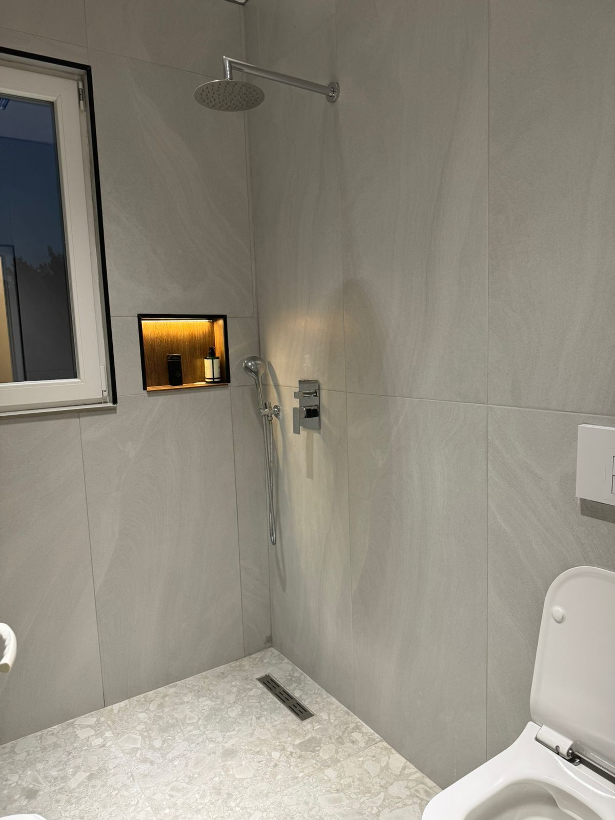 A modern bathroom with a shower, toilet, and a small window.