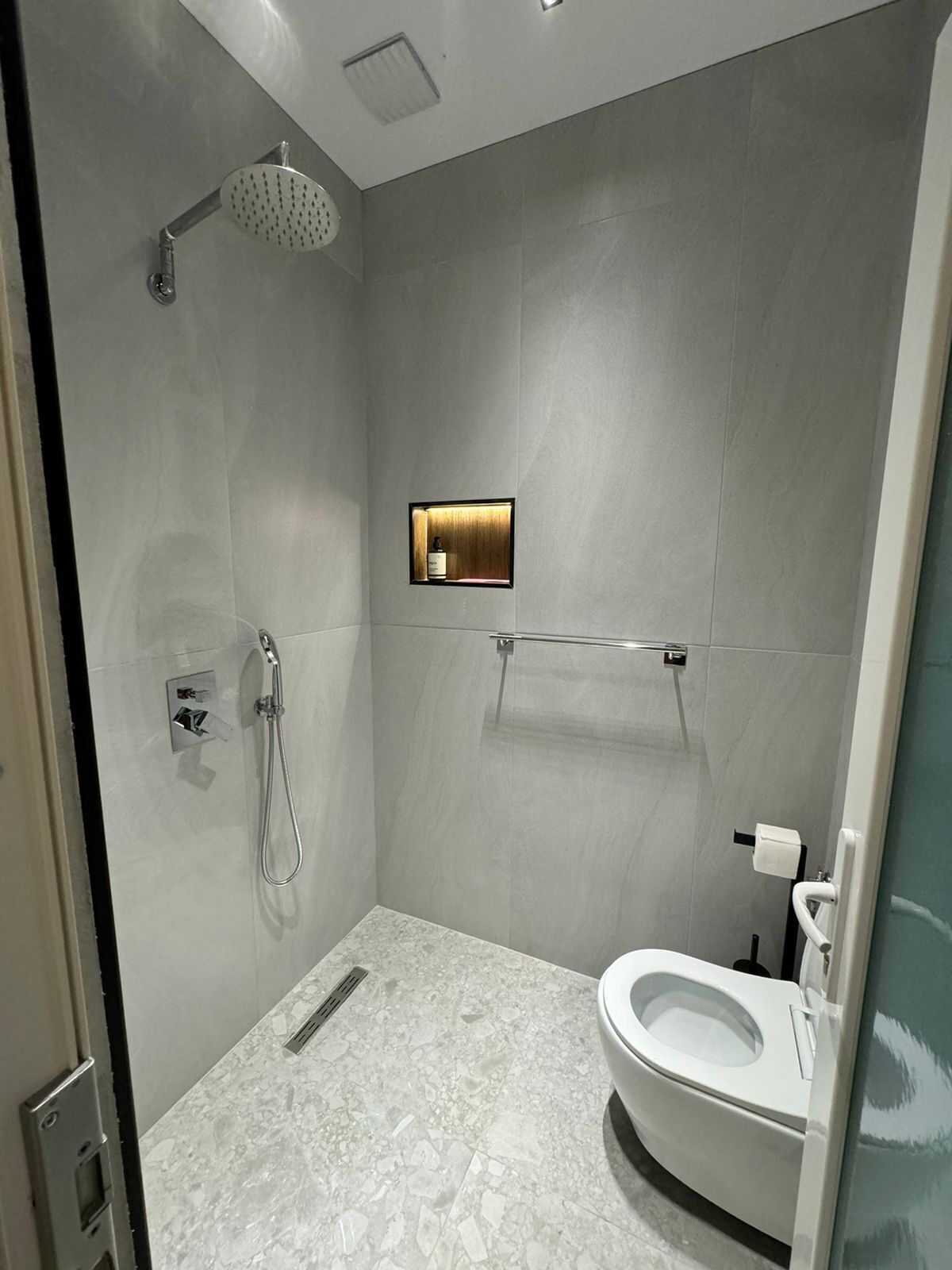 A modern bathroom with a shower, toilet, and a small mirror.