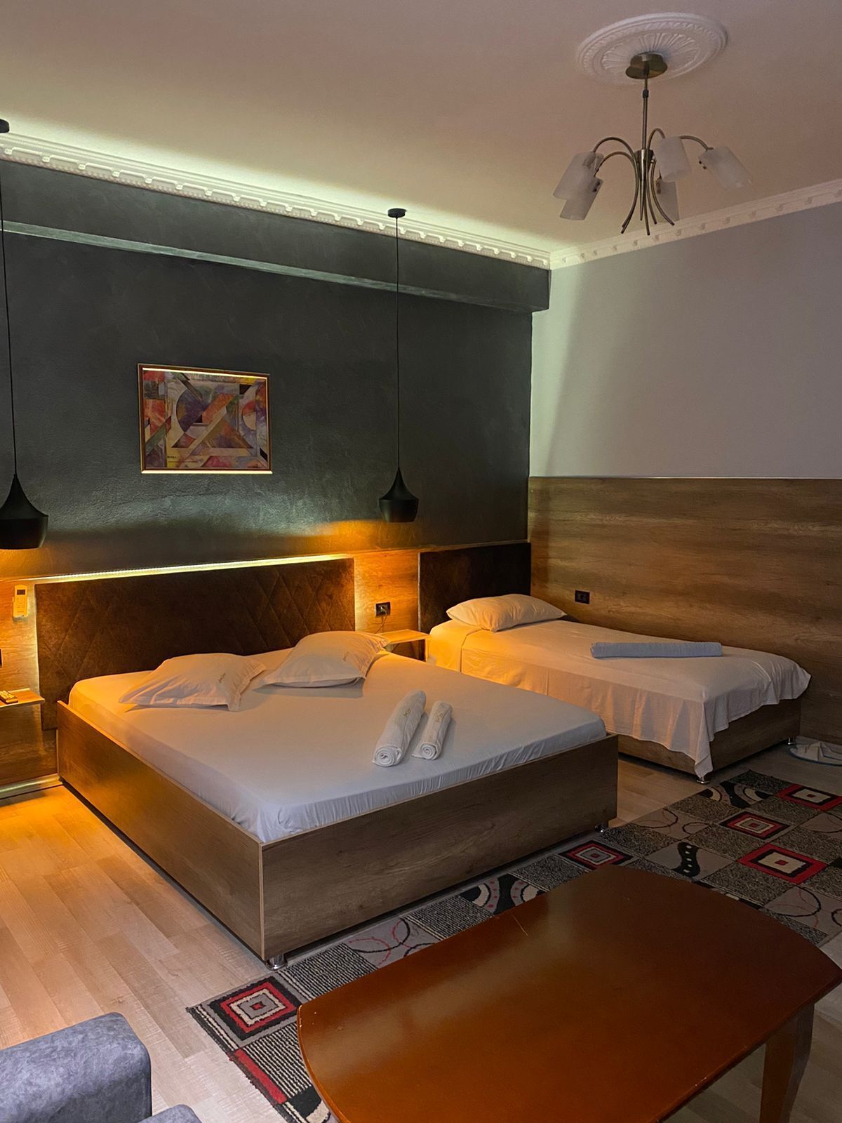 Ein Hotelzimmer mit zwei Betten, einem hölzernen Kopfteil, einem Bild an der Wand und einem gemusterten Teppich.