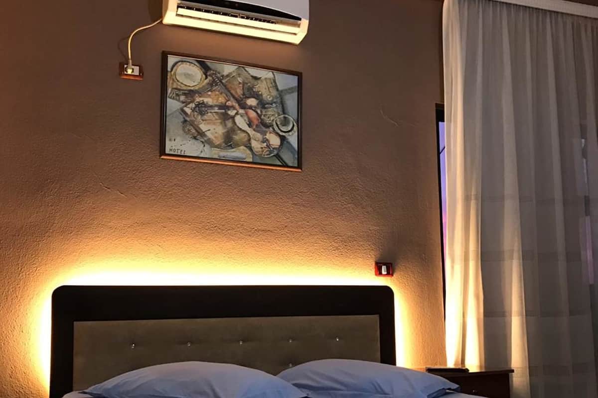 A hotel room with a bed, an air conditioning unit, a painting, and a curtain.