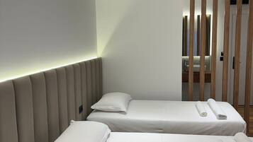 Une chambre d’hôtel moderne avec deux lits simples, une table de chevet ronde blanche et une cloison en lattes de bois.