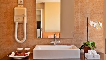 A bathroom with a white sink, a mirror, a handheld showerhead, a potted orchid, and a tissue box.