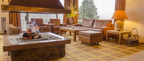 Ein gemütliches Wohnzimmer mit Kamin aus Stein, Ledersofas und einem Karo-Boden.