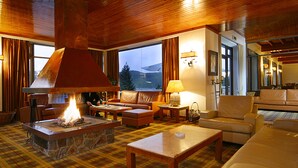 Una sala de estar acogedora con chimenea de piedra, sofás de cuero y un amplio ventanal con vistas al exterior.