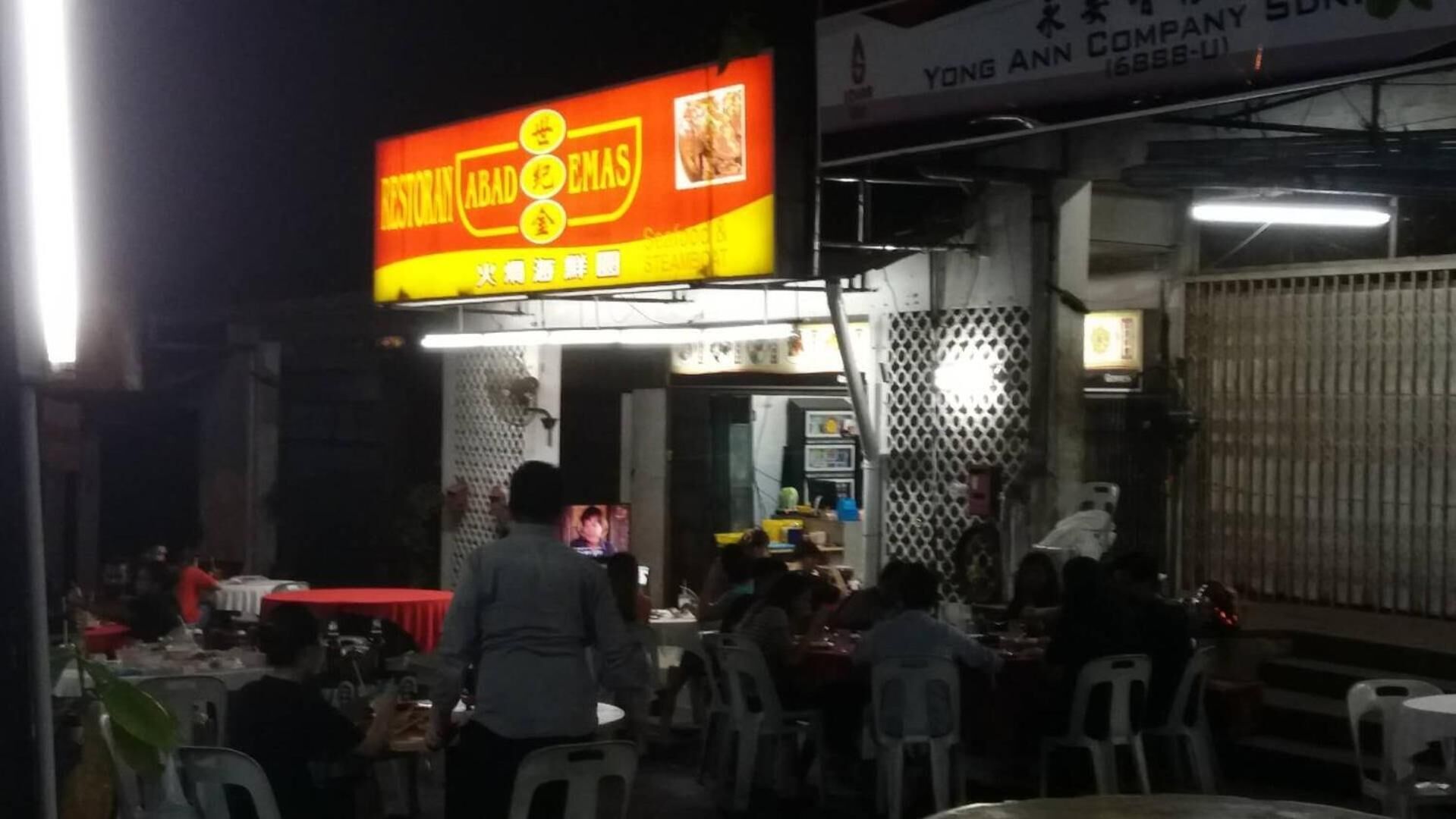 An outdoor dining area with tables and chairs, a bright sign for a restaurant, and a partially visible building with a window.