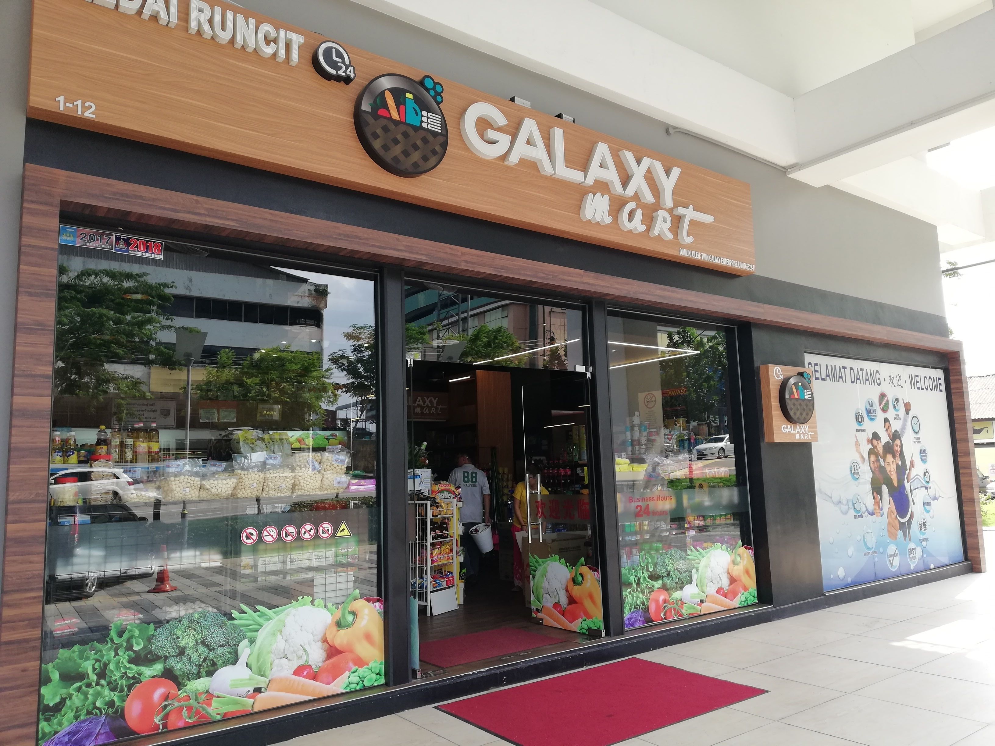 A Galaxy Mart store with a large sign, large windows displaying fresh produce, and a red carpet outside.