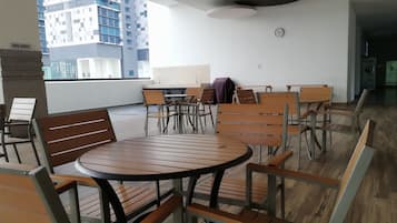 A modern indoor seating area with round tables and wooden chairs, a clock on the wall, and a view of a high-rise building.