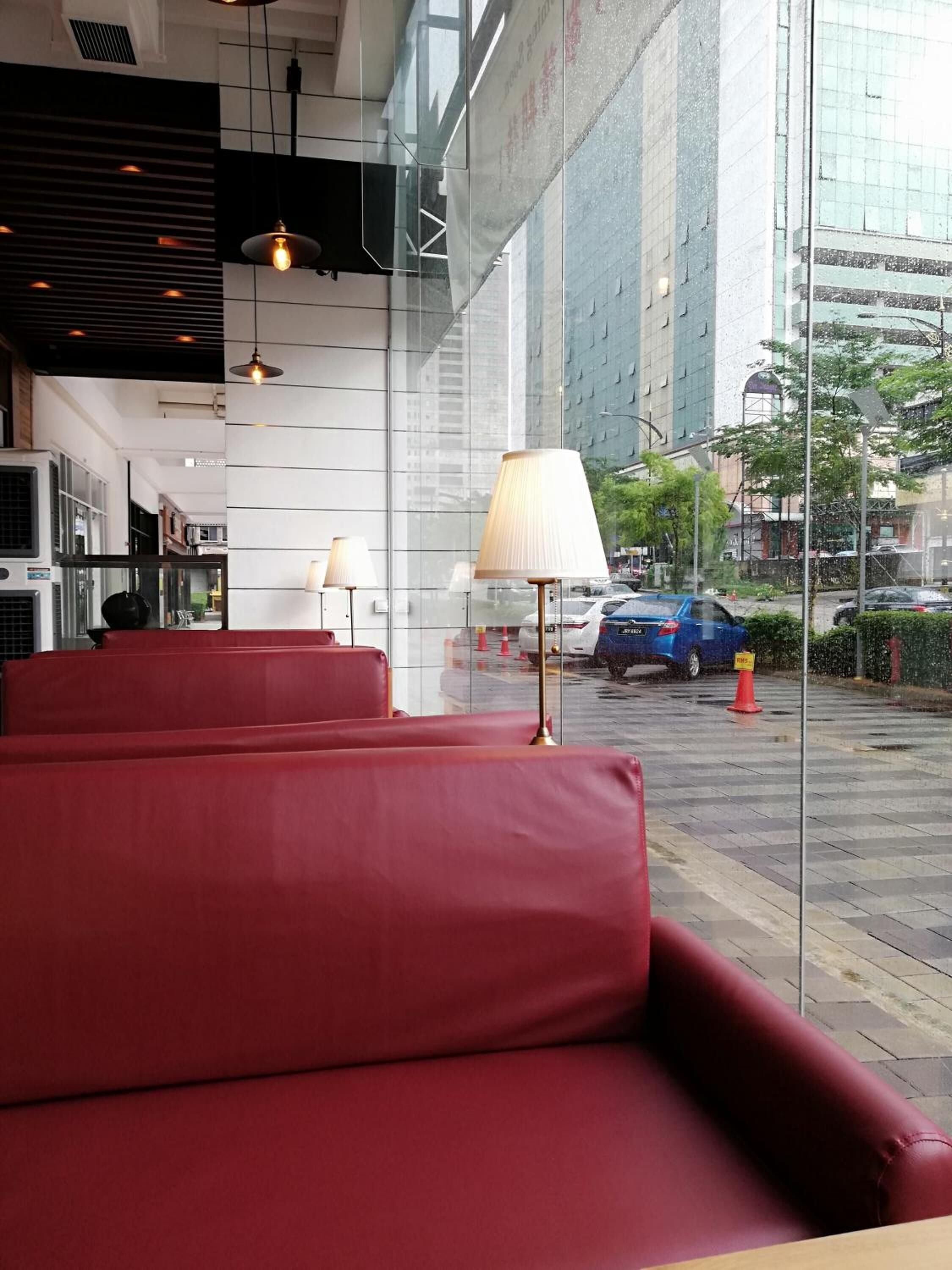 A restaurant with red cushioned seating, hanging pendant lights, and a view of the street through large windows.