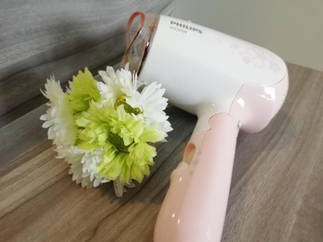 A Philips hair dryer on a wooden surface with a bouquet of white and green flowers beside it.