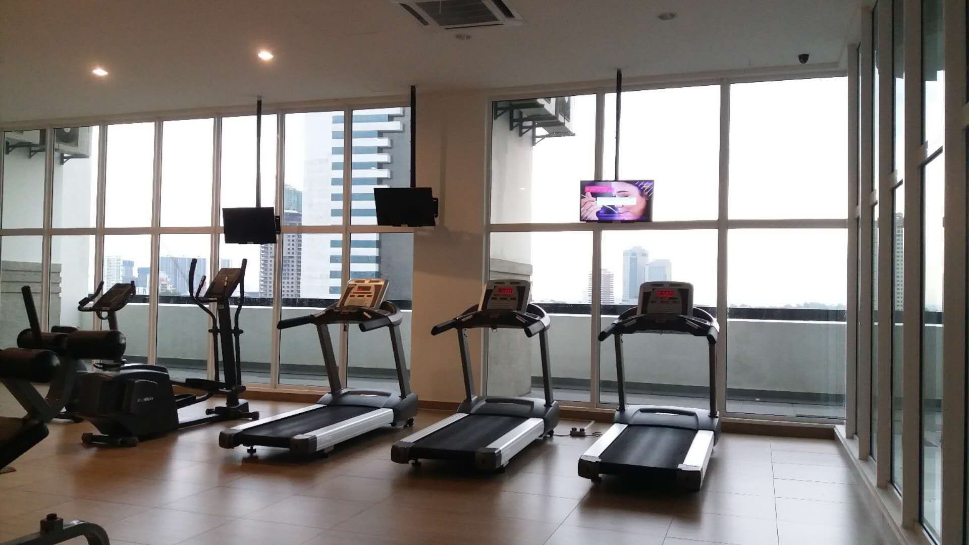 A gym with treadmills, stationary bikes, and weight machines, large windows with a city view.