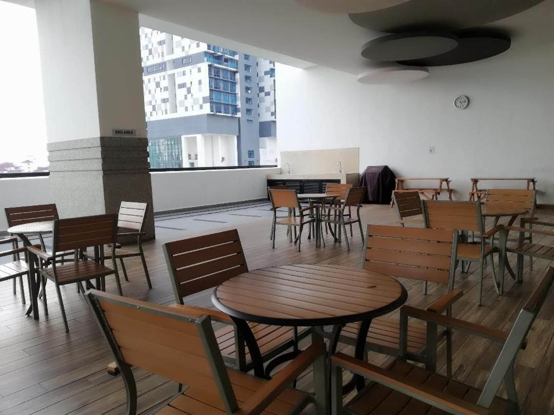 Una terraza en la azotea con mesas y sillas de madera, vistas de un edificio moderno y un reloj en la pared.