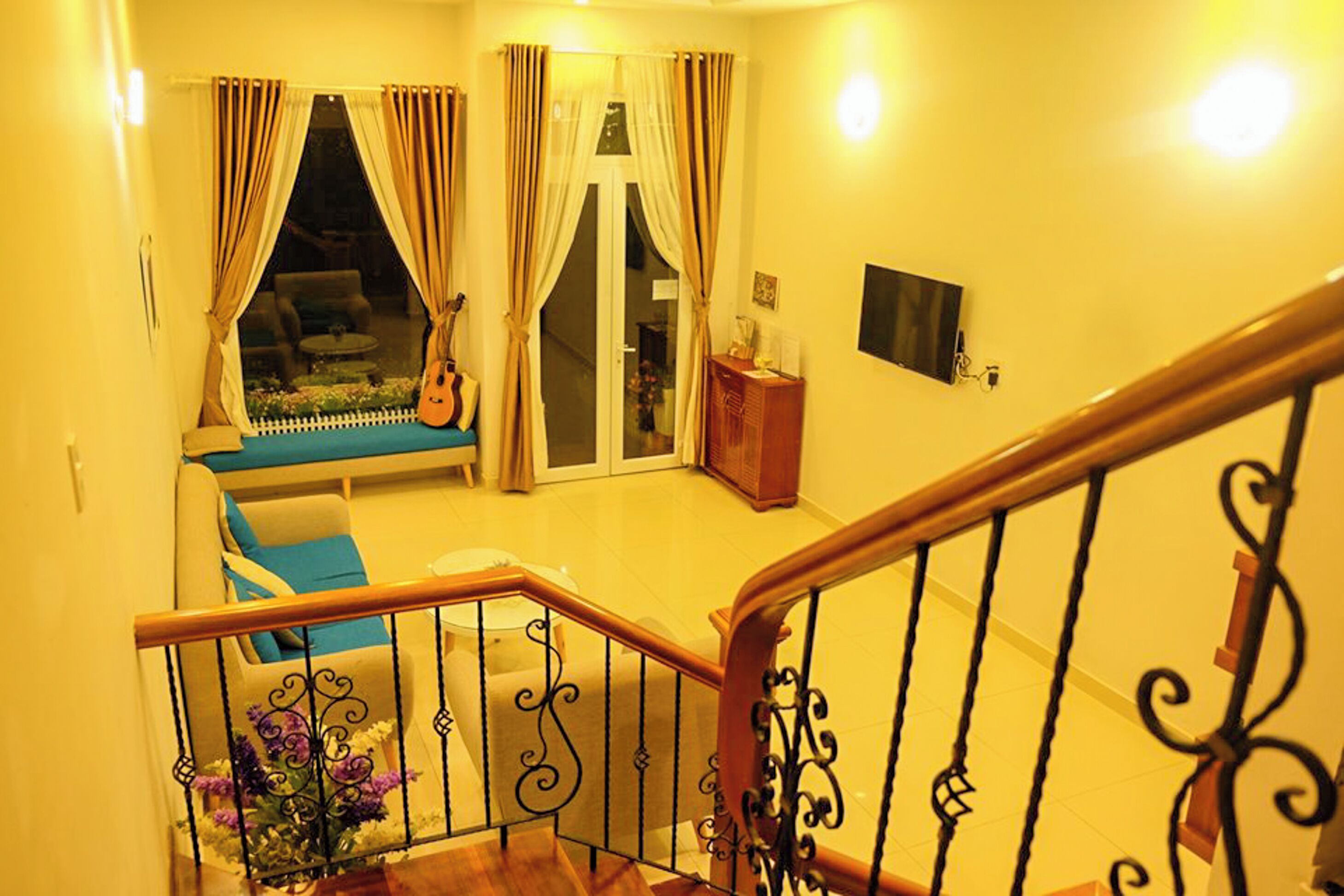 A staircase with ornate black railings leading to a room with a sofa, a guitar, and a television.