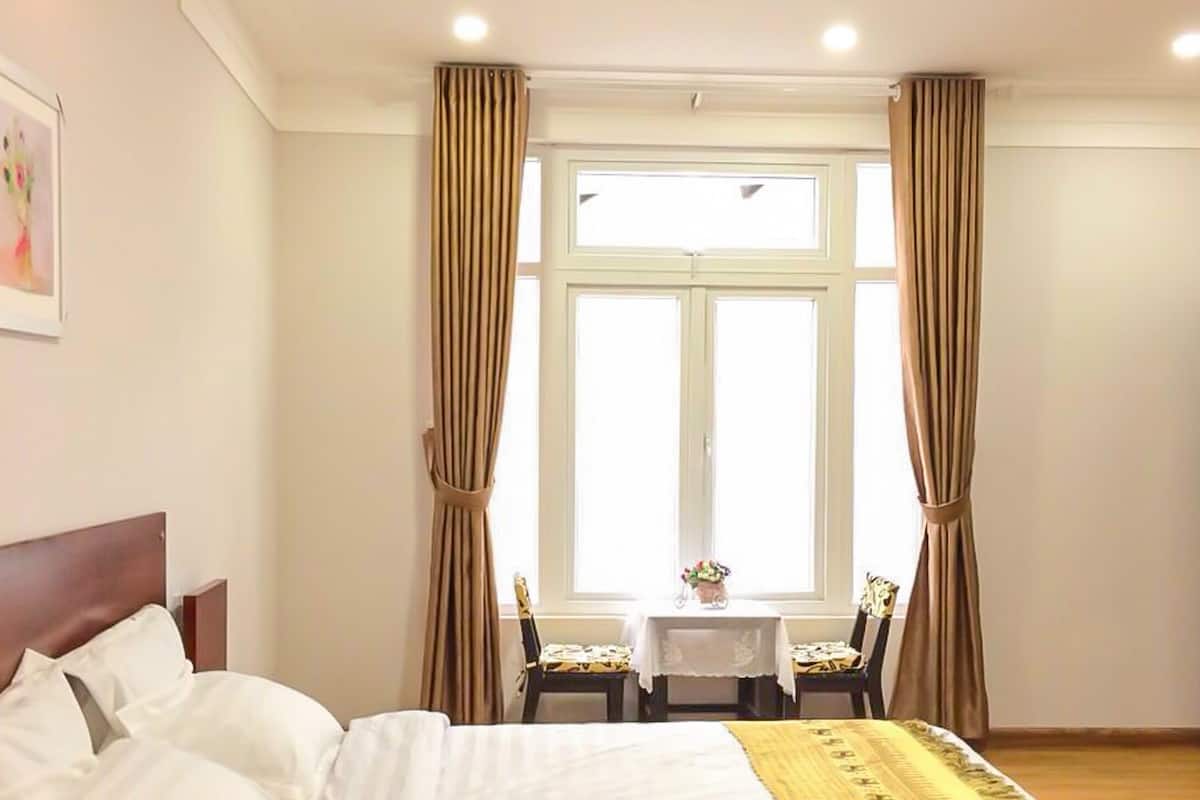 A hotel room with a bed, a small table with chairs, and a window with curtains.
