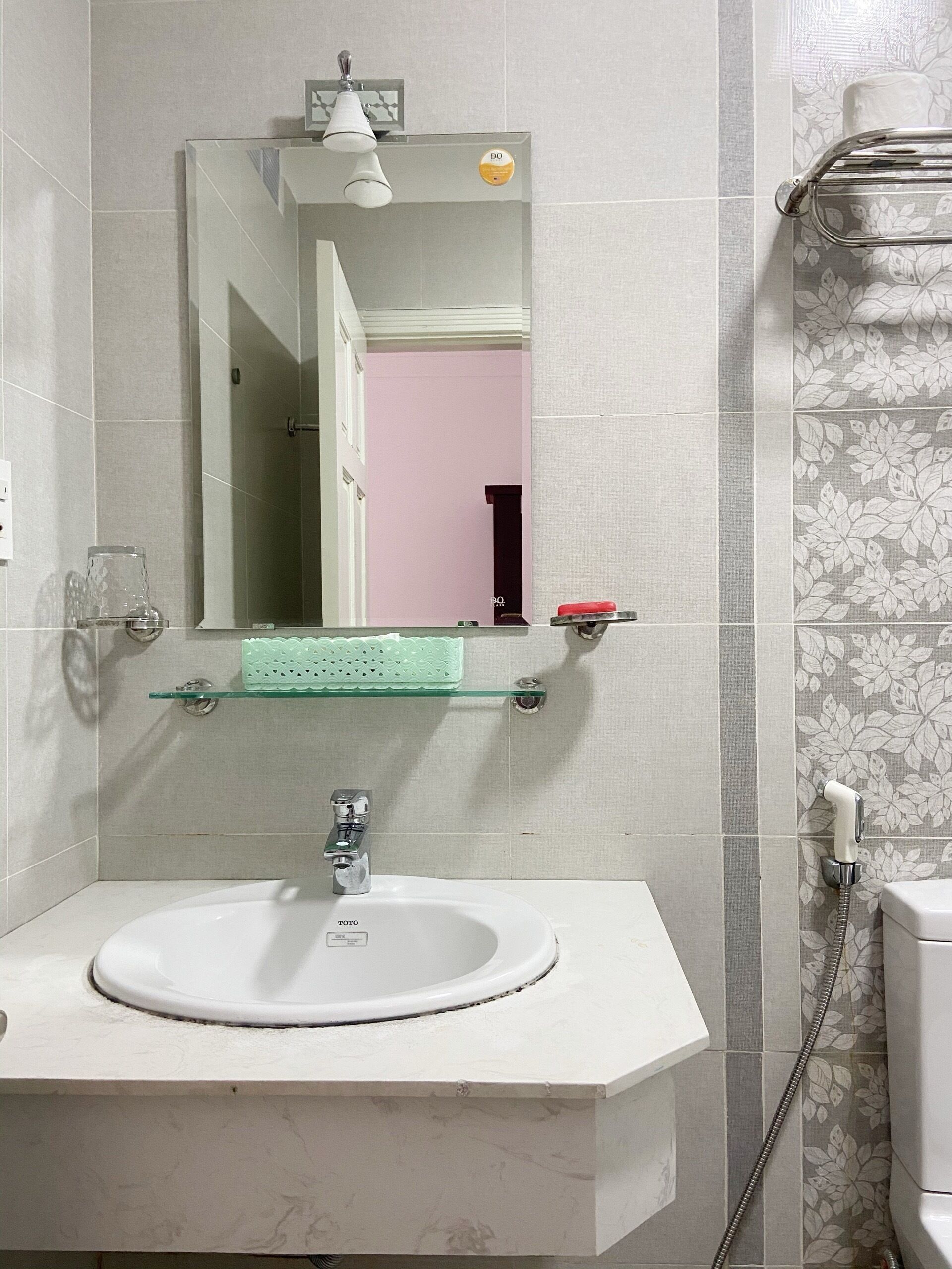 Une salle de bain avec un lavabo blanc, un miroir, une étagère en verre et un espace douche.